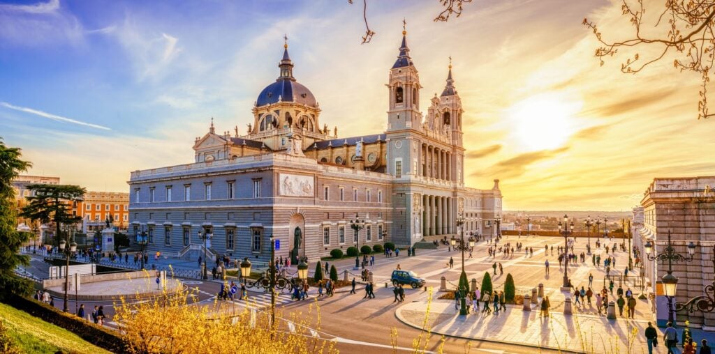 Sunset view of Madrid's Almudena Cathedral and Royal Palace with pedestrians crossing the plaza