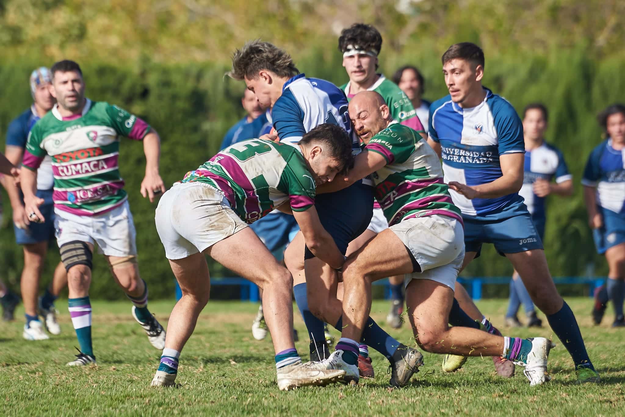 Rugby players in a tackle on a grass field in Spain.