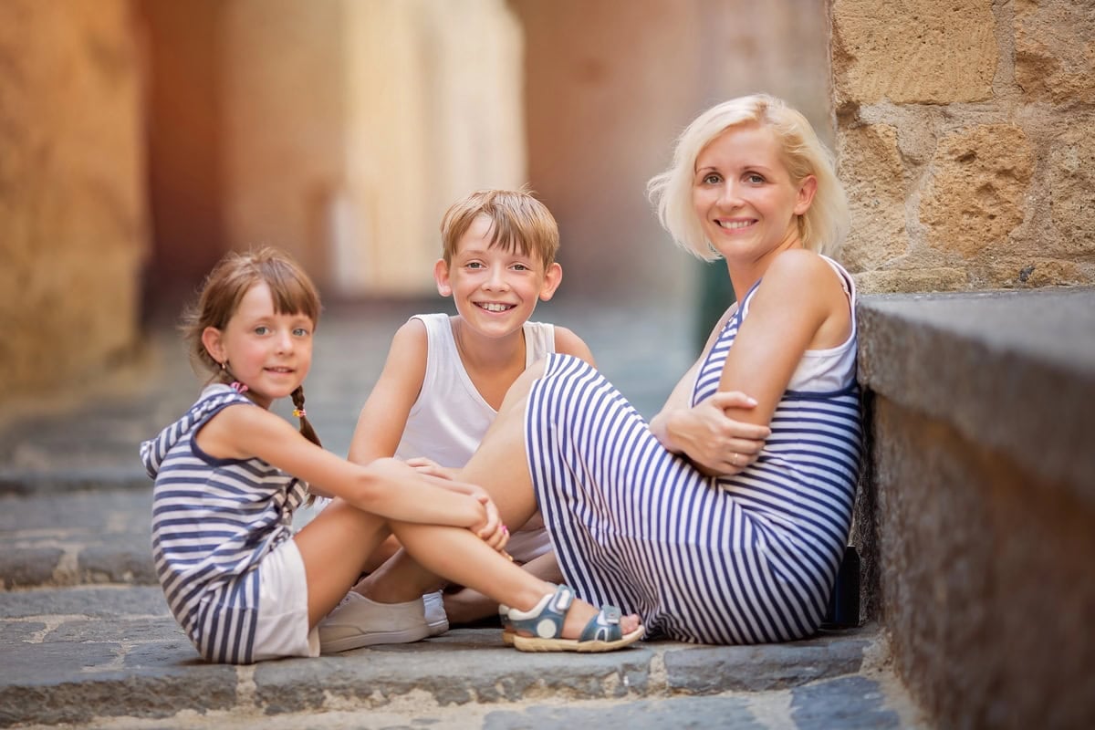 Mother and two sons sitting on the floor in a street in Spain